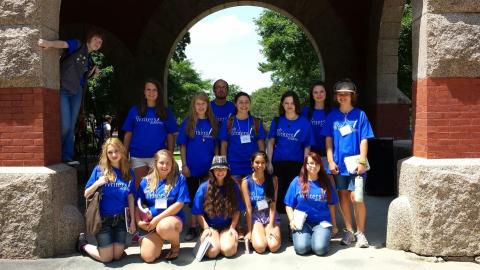 A photo of students wearing blue Writers Academy shirts standing under the arch in front of T Hall