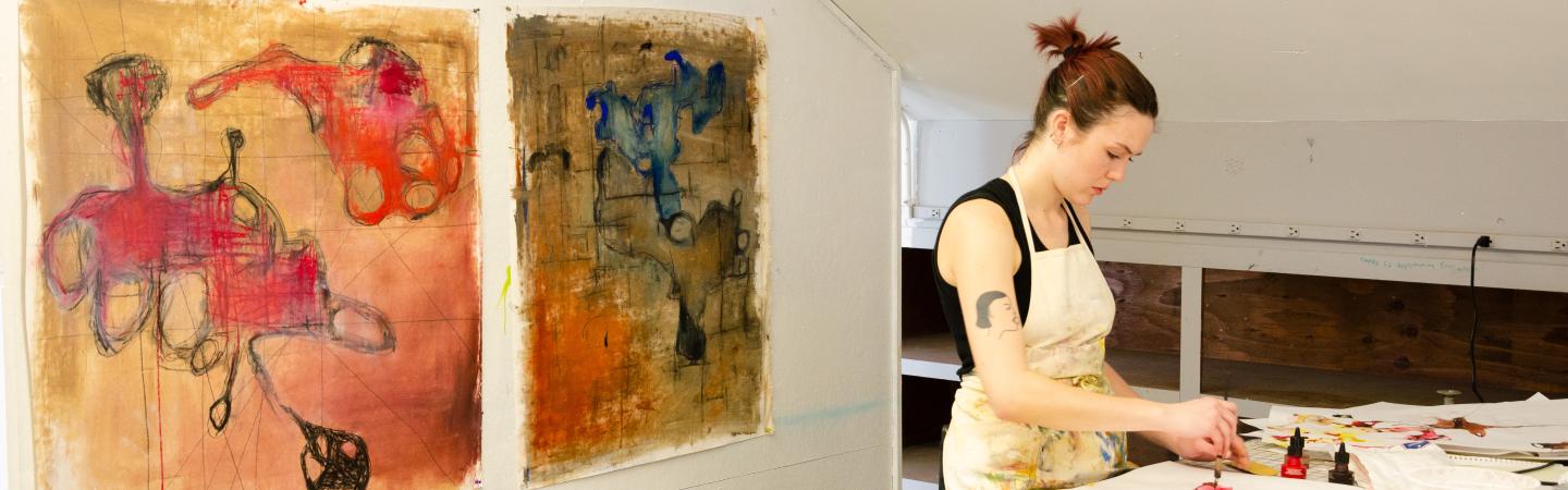 Art student in her studio with two paintings behind her