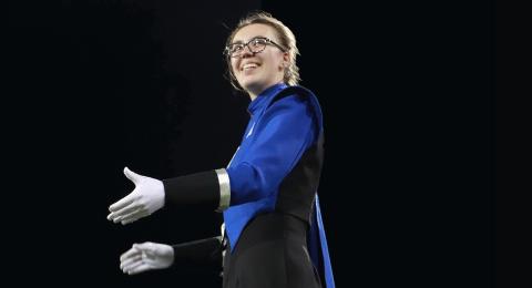 Marching band drum major in blue and black UNH uniform with white gloves in front of a dark night sky