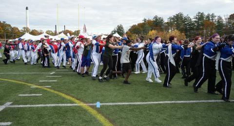 Members of multiple high school marching bands do a conga line in Wildcat Stadium