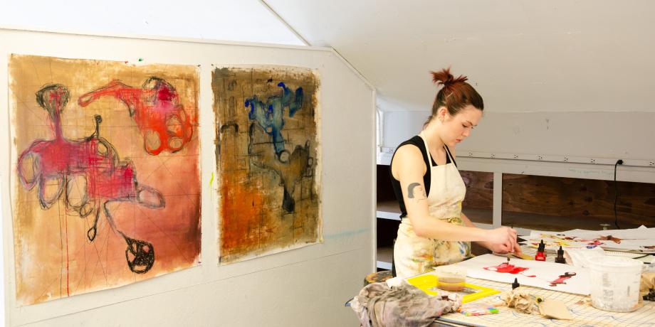 Art student in her studio with two paintings behind her