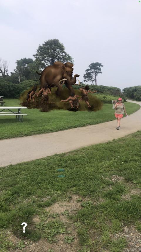 individual walks along path at Odiorne State Park with overlay image of woolly mammoth hunt visible behind her from the app