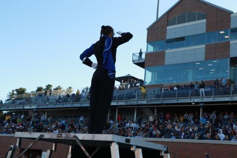 Marching band drum major saluting the crowd atop the podium at a UNH performance