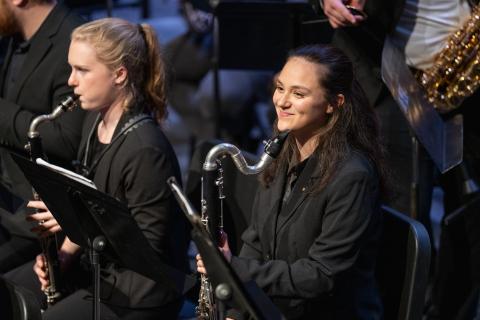 Wind Symphony bass clarinet player smiles next to alto clarinetist playing instrument