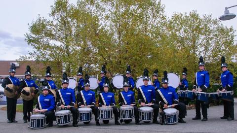 Posed picture of the 2023 WMB drumline in front of a tree with yellow leaves