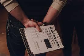 A person holding a clipboard behind their back. Clipboard had a paper with the heading "Slam Free or Die" on it.