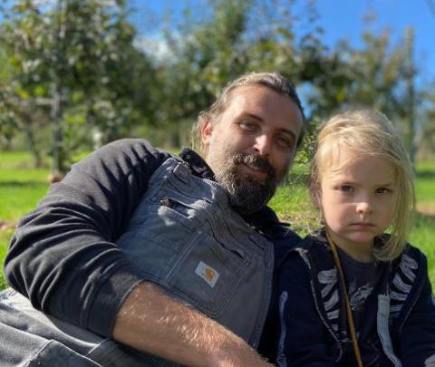 Organic farmer Craig Jenson sitting outdoors in overalls with son.
