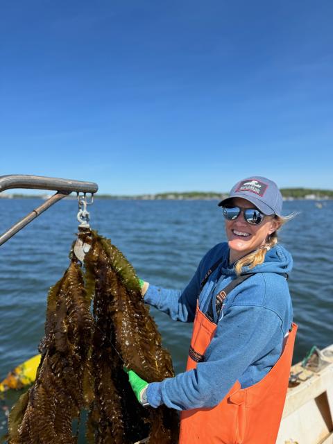 Inga Potter of Cold Current Kelp on a boat, smiling, and holding a large piece of kelp.