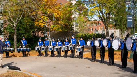 Marching band drumline battery warms up in an arc on game day with fall leaves behind them
