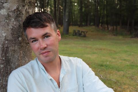 Portrait of Benjamin Phinney leaning against a tree and smiling