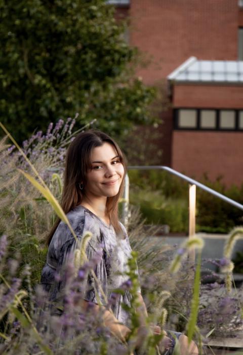 EdD student emma green sitting on steps, smiling at the camera, with wildflowers in the foreground and background