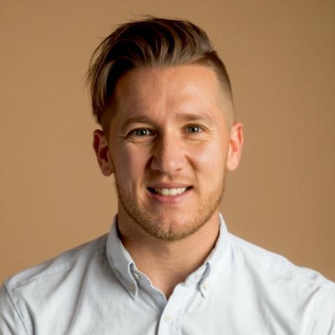 EdD student Jon Luszcz smiling directly at camera in front of a beige background